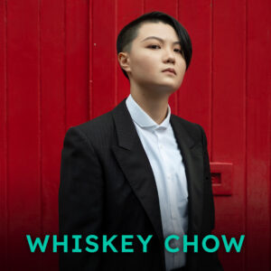 Photograph: A head and shoulder close up of an East Asian person with their face looking slightly to the right, in front of a red background. Their black hair is shaved on the right side and falls to their cheek on the other. They are looking straight at us. They are wearing a smart white shirt and jacket. On top of the photograph is the text 'Whiskey Chow' in green lettering.