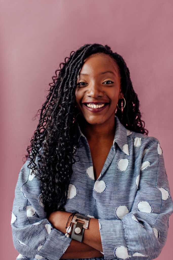 Nassy is a Black woman with long black hair with loose curls, a big smile and burgundy lippy on.