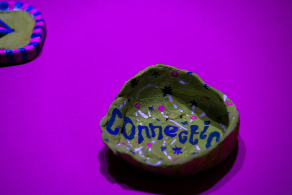 A small handmade clay pot, on a purple background, with the word 'Connection' written on it with paint and small colourful illustrations.