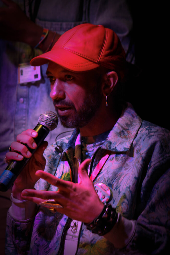 A man in a red hat (Tarik Elmoutawakil) speaks into a microphone.